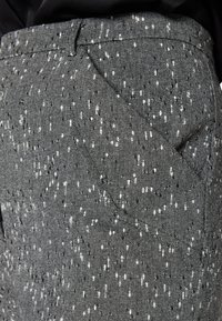 Tissu gris à motifs avec de petites taches blanches et noires. Design ajusté avec une poche latérale et une texture lisse.