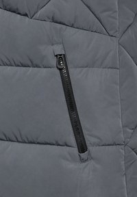 Graue Steppjacke mit einem Reißverschlussfach, gestepptem Design, glatter Textur und schwarzem Reißverschluss.