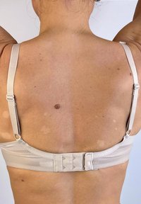 Sujetador beige visto desde la parte posterior, con tirantes ajustables, un cierre de gancho y ojo, y tejido suave con un sutil brillo.