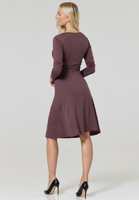 Long-sleeve, A-line dress in muted mauve, made from soft material. Features a round neckline and a flared hem. Worn with black high-heeled shoes.