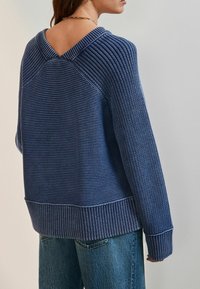 Blå strikket sweater med bred V-udskæring og ribbet kant. Designet har horisontale striber og løstsiddende ærmer.