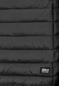 Schwarze Pufferjacke mit gestepptem Design, aus strukturiertem Stoff, sichtbaren Nähten und einem kleinen Etikett mit "Sublevel" an der Seite.