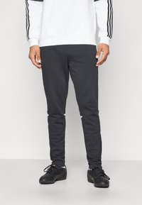 Dark gray jogger pants with a slim fit, featuring white side stripes and elastic waistband. Material appears soft and textured.