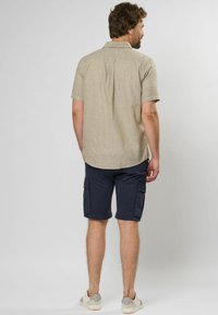 Kortærmet beige skjorte med en subtil tekstur og krave, parret med marineblå cargo shorts med sidelommer og længde under knæet.
