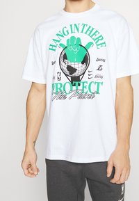 Biała bawełniana koszulka z grafiką zielonej dłoni na globusie, z napisem "HANG IN THERE PROTECT The Paint" w kolorze teal.