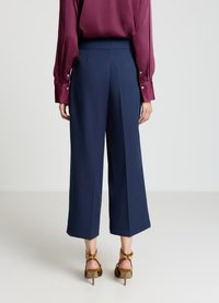 Pantalon large marine à taille haute avec des plis, associé à un chemisier en soie bordeaux avec des poignets boutonnés et des manches ajustées.