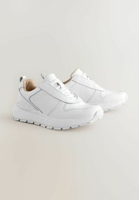Hvite sneakers med en overdel i lær, rund tå, elastisk bånd og gummisåle. Teksturerte detaljer med en glatt finish. Enkel og moderne design.