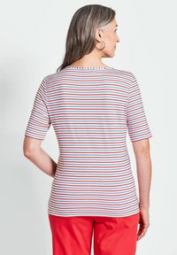 Le t-shirt rayé présente des rayures horizontales rouges, bleues et blanches, des manches courtes et un col rond. La vue arrière montre une légère courbure à l'ourlet.