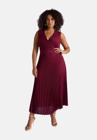 Robe midi plissée bordeaux avec un décolleté en V profond et une taille ajustée, fabriquée à partir d'un tissu léger. Présente une silhouette fluide et des talons spaghetti.