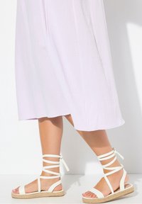 Weiße Riemchensandalen mit Knöchelriemen, aus weichem Material und mit einer mit Jute umwickelten Sohle. Getragen mit einem hell-lavendelfarbenen Kleid.