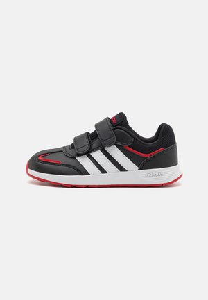 Black athletic shoe with two adjustable Velcro straps, white side stripes, red accents, and rubber sole. Features a textured upper for support.