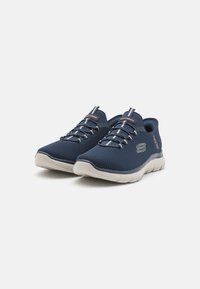Baskets de sport bleu marine avec tige en mesh, lacets élastiques et semelle flexible de couleur claire. Présente un logo discret sur le côté.