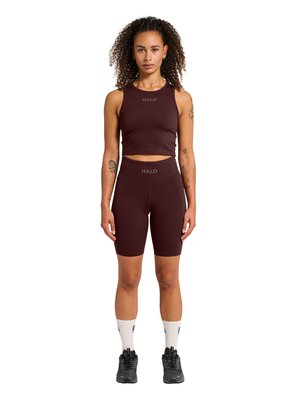 Kvinde stående med front mod, iført mørkebrun ærmeløs crop top og matchende højtaljede cykelshorts med hvide sokker og sorte sneakers.