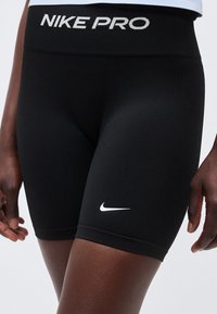 Gros plan sur une personne portant un short de compression Nike Pro noir avec le logo swoosh blanc sur la cuisse et le texte Nike Pro sur la ceinture.