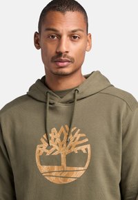 Hoodie khaki in cotone misto, con un grande logo ad albero di colore marrone chiaro. Include cappucci e ha un design dal taglio rilassato.