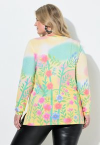 Bluzka z długim rękawem z miękkiej tkaniny, z pastelowym kwiatowym wzorem w różowe, niebieskie i zielone akcenty na żółtym tle. Z boku rozcięcia.