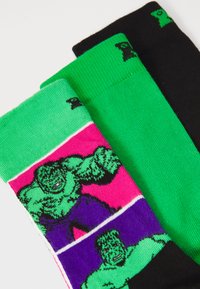 Three pairs of socks featuring vibrant colors: green with a Hulk graphic on pink, solid green, and solid black. Distinctly patterned and textured.