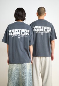 Gray cotton t-shirts with a large white "VERTERE BERLIN" logo on the back, paired with textured, patterned light blue snake print pants.