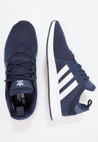 Ett par marinblå Adidas-sneakers med vita tre ränder, mesh-överdel och vit sula, visat från ovan- och sidovy.