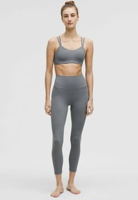 Grijze sportbeha met dunne bandjes en bijpassende high-waisted legging, beide gemaakt van soepel, rekbaar materiaal, geschikt voor actieve kleding.