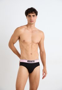 Black brief underwear with a pink elastic waistband featuring the "DIESEL" logo in black. Smooth fabric, fitted design, and a minimalist style.