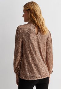 Bronze sequin top with long sleeves, high neck, and back keyhole detail; features a textured, shimmering surface and elastic cuffs.