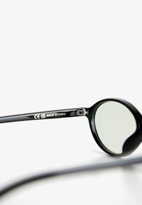 Fekete napszemüveg lekerekített lencsékkel, elegáns műanyag kerettel, a szárán jól látható gravírozással, könnyű kialakítás, Kínában gyártva.