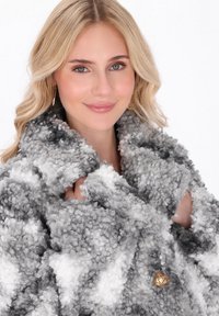 Cappotto oversized e fluffy con toni grigi e bianchi, texture morbida e decorato con un bottone dorato. Design caldo e accogliente con un ampio colletto.