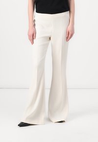Pantalons à jambes larges en tissu beige clair, présentant une texture lisse et une coupe ajustée, associés à des escarpins noirs à bout pointu.
