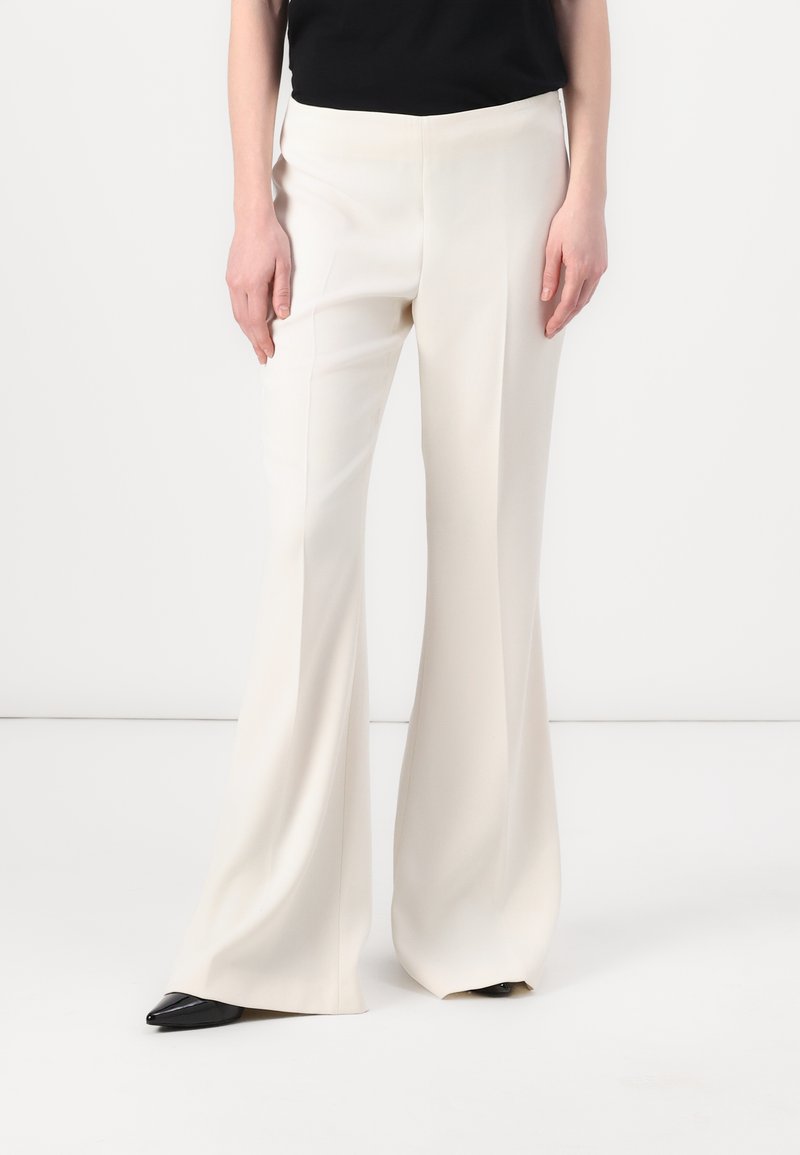 Pantalons à jambes larges en tissu beige clair, présentant une texture lisse et une coupe ajustée, associés à des escarpins noirs à bout pointu.