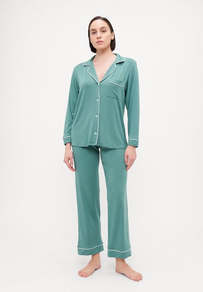 Pajama set in soft teal fabric. Long-sleeve top with button closure and chest pocket, paired with matching wide-leg pants featuring white trim.