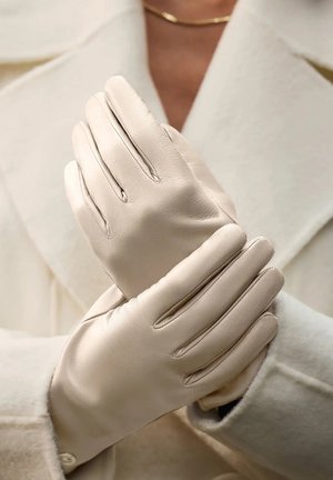 Beige leren handschoenen met een gladde textuur, voorzien van vijf vingers en subtiele stikdetails, tentoongesteld tegen een lichtgekleurde jas.