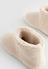 Chaussons en polaire rose pâle avec une texture douce, un dessus arrondi et une doublure intérieure douce. Ils présentent une semelle en caoutchouc légère et lisse.