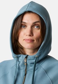 Lichtblauwe zip-up hoodie met een trekkoordcapuchon, met een zachte textuur, gouden hardware en stikdetails langs de naden.