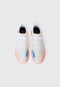 Une paire de chaussures de sport blanches avec des accents bleus et oranges et des lacets blancs, vue de dessus sur un fond blanc.