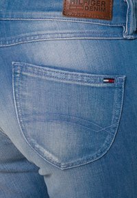 Ljusblå denimjeans med en bakficka som har en rundad söm och en liten logolapp i rött, vitt och blått på sidan.