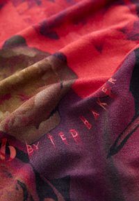 Textiel met een kleurrijke bloemenprint in rood, roze en groen op een donkere achtergrond, met een gladde, zachte textuur.