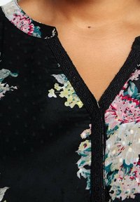 Gros plan d'un chemisier noir à motifs floraux avec un col en V bordé de dentelle noire sur la partie supérieure de la poitrine et le cou d'une personne.