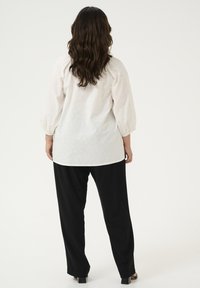 Bijela teksturirana bluza s napuhanim rukavima u paru s lepršavim crnim hlačama. Bluza ima suptilne uzorke i opušten kroj.