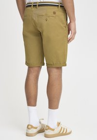 Shorts din bumbac khaki, cu manșete răsucite, buzunare spate cu închidere prin buton și un etichetă pe banda din spate; asortați cu adidași bej și șosete albe.