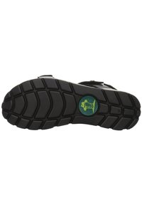 Semelle de sandale en caoutchouc présentant un motif texturé avec des rainures profondes, de couleur noire, et un logo circulaire vert avec une icône de chien.