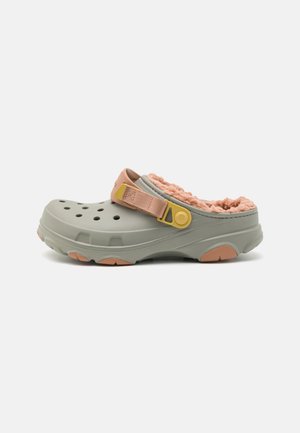 Sabot gris clair à enfiler avec doublure pelucheuse pêche, trous de ventilation et bride de talon réglable pêche et jaune sur fond blanc.