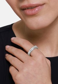 Anello in argento con pietre rettangolari, banda texturizzata, indossato su una mano che tocca delicatamente il collo. Colore della pelle visibile, l'abbigliamento è scuro.
