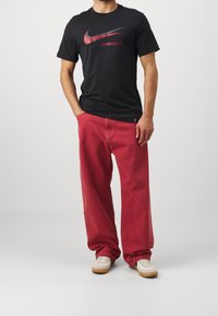 Musta T-paita, jossa punainen Nike-logo ja teksti "LIVERPOOL FC", yhdistettynä väljiin punaisiin housuihin ja valkoisiin tennareihin, joissa on kumipohjat.