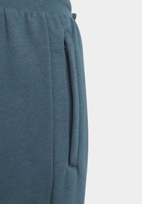 Blå joggerbyxor gjorda av mjukt tyg, med sidoficka med dragkedja och elastisk midja för komfort. Ytan har en slät textur.