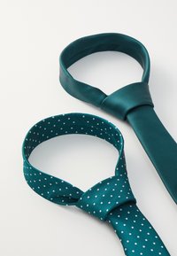 Două cravate teal expuse; una solidă cu textură ribbed, cealaltă cu buline albe, amândouă având un design clasic.