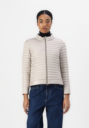 Beige boblejakke med horisontal søm, høy krage og frontglidelås. Båret over en svart topp, sammen med mørkeblå jeans.