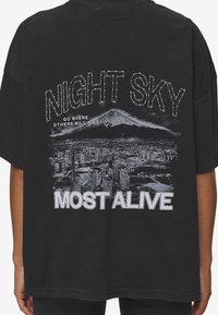 Svart bomull t-shirt med en grafisk utskrift av en stadssilhuett och berg. Texten säger "NIGHT SKY" och "MOST ALIVE" i vitt.
