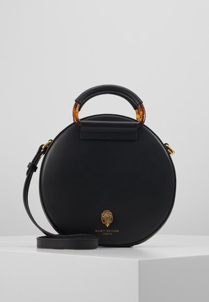 Sac à main rond en cuir noir avec poignée supérieure en écaille de tortue et noire, accents dorés et bandoulière amovible sur surface blanche.
