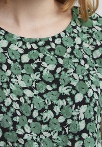 Musta kangas, jossa on kukkakuvio vihreillä lehdillä ja kukilla. Kuviolla on sileä pinta ja pyöreä kaula-aukko.